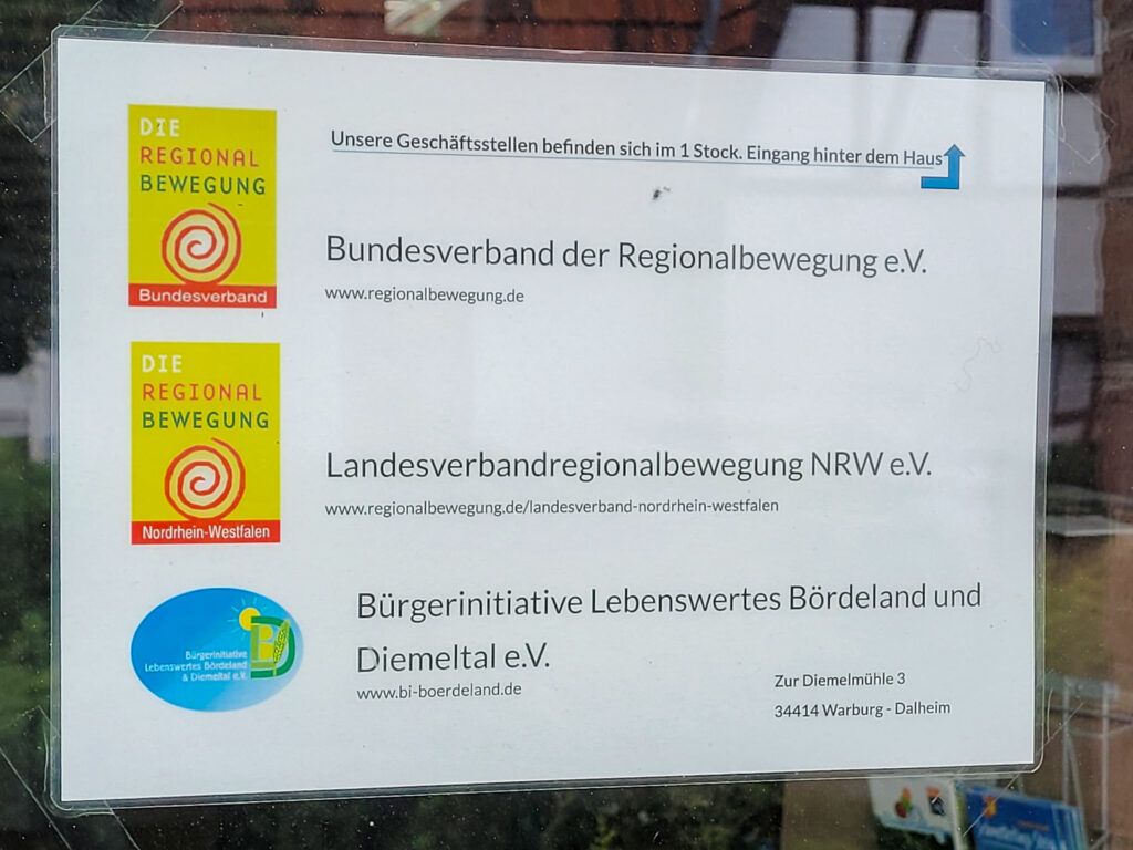 Hinweisschild mit Logos der Regionalbewegung und der BI an der Alten Schule in Dalheim.