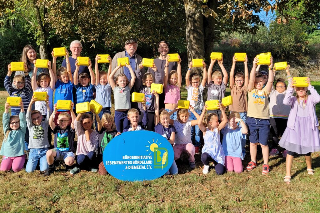 Grundschulkinder recken freudig ihre gelben Bio-Brotboxen in die Höhe.