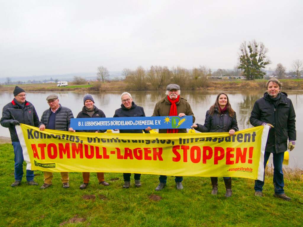 Mitglieder der BI Lebenswertes Bördeland & Diemeltal mit gelben Banner und Aufschrift "Atommüll-Lager-Stoppen" an der Weser.