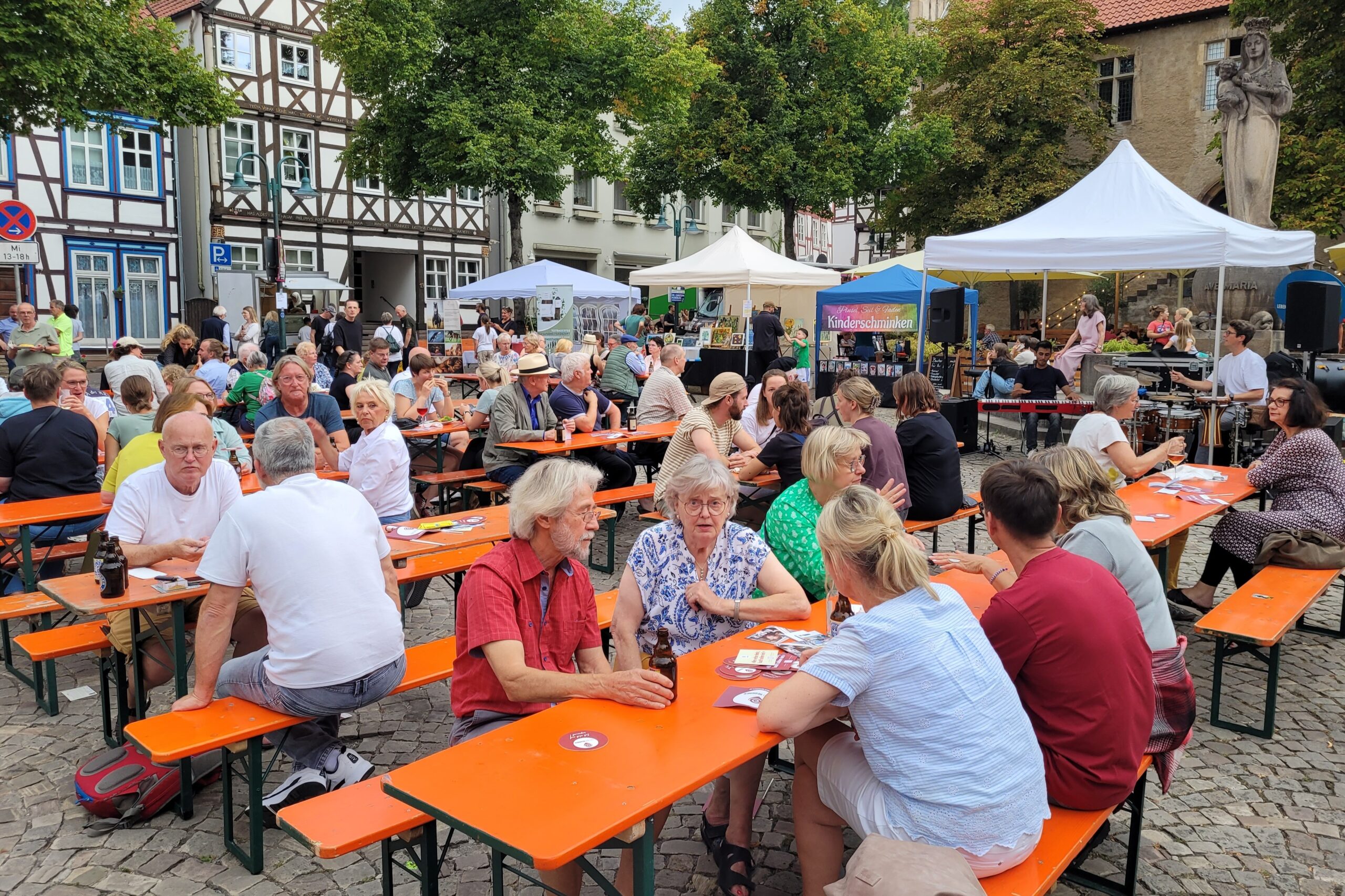 Menschen auf dem Marktplatz lauschen an Tischen der Musik.