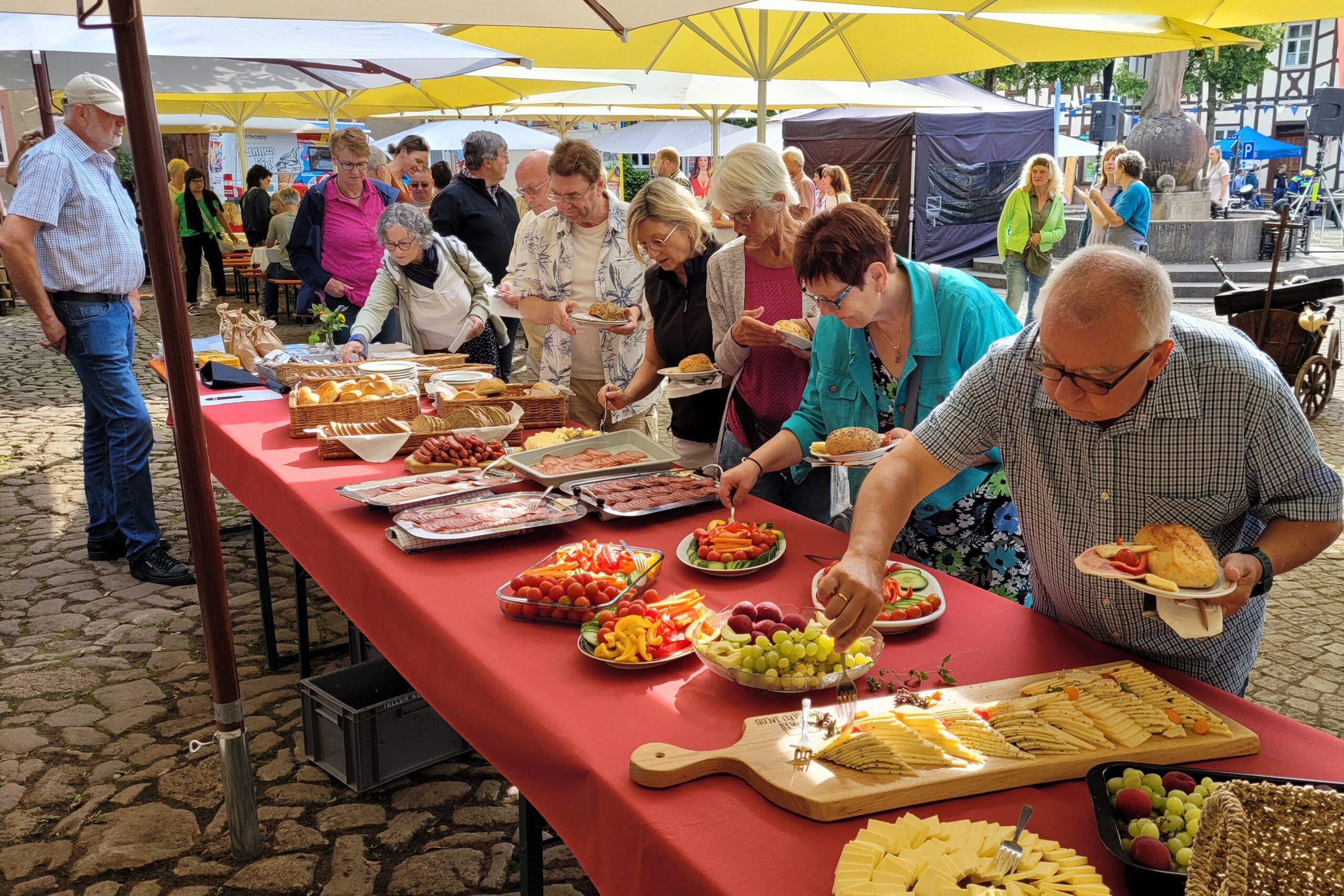 Besucher an einem langen roten Tisch wählen ihr Frühsstück aus.